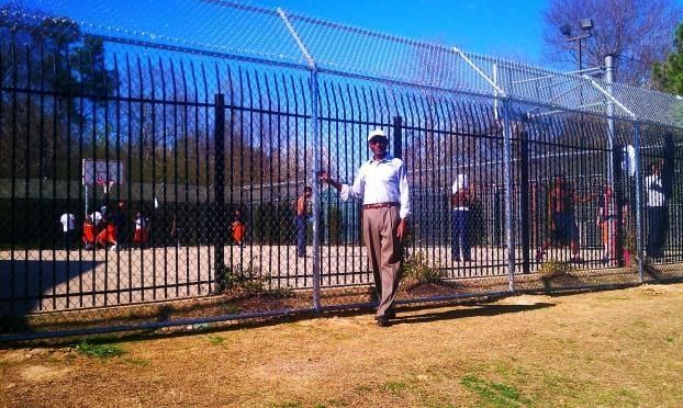 A man is standing in front of a fence in a park.