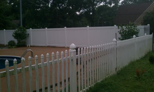 A white picket fence surrounds a swimming pool in a backyard.