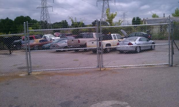 A lot of cars are parked behind a chain link fence