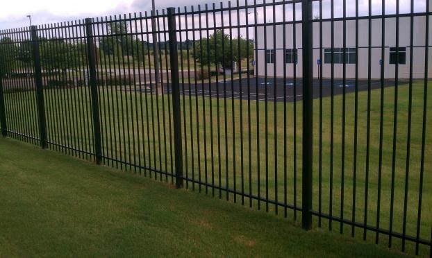 A black metal fence surrounds a lush green field.