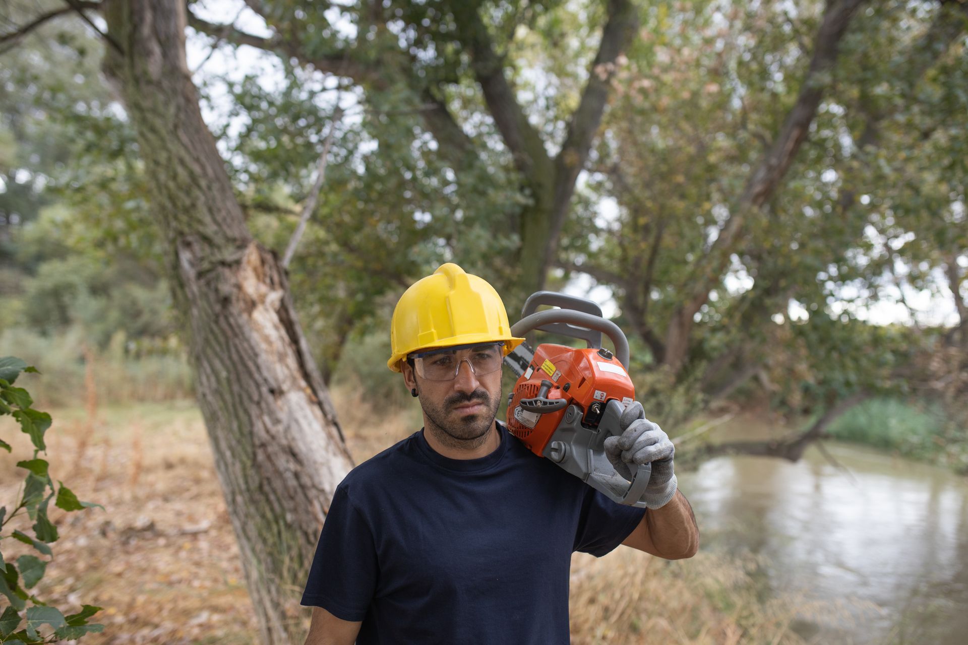 A man wearing a hard hat and gloves is holding a chainsaw.