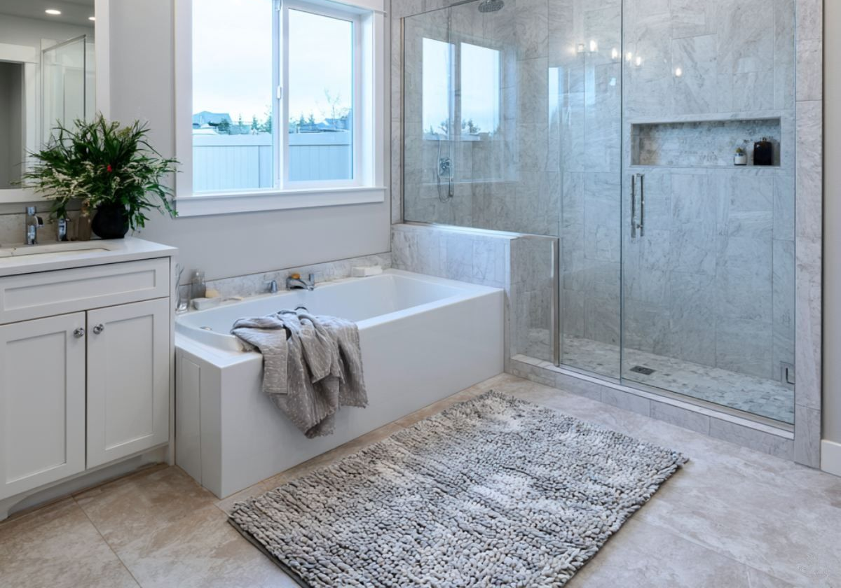 Bright modern bathroom with a freestanding tub, glass shower, white vanity, and gray rug.