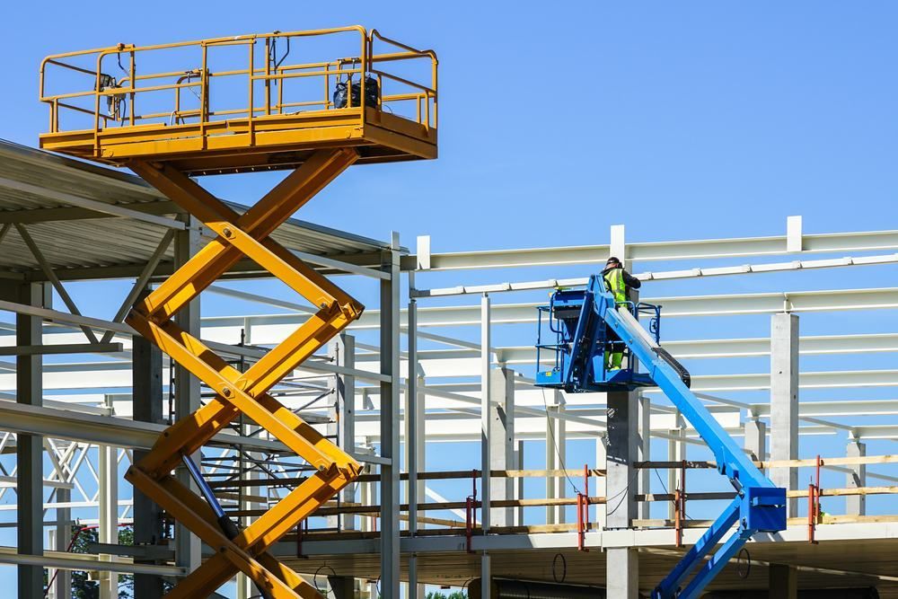 A Man Is Working On A Scissor Lift At A Construction Site — Port Stephens Cranes In Salt Ash, NSW
