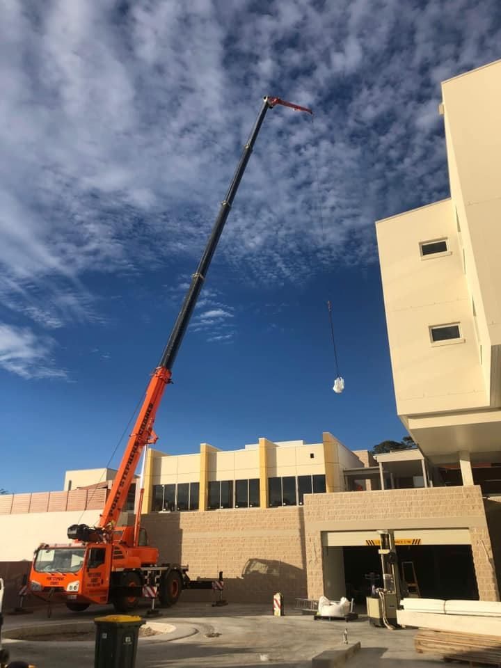 A Large Orange Crane Is Lifting Something In Front Of A Building — Port Stephens Cranes In Salt Ash, NSW