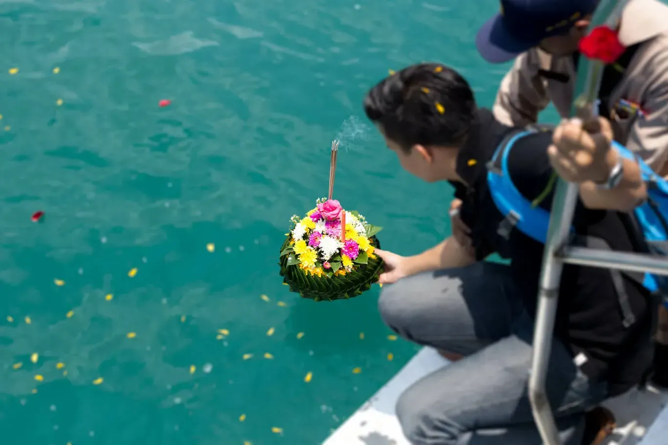 Person on a boat lowers a flower-covered offering into turquoise water