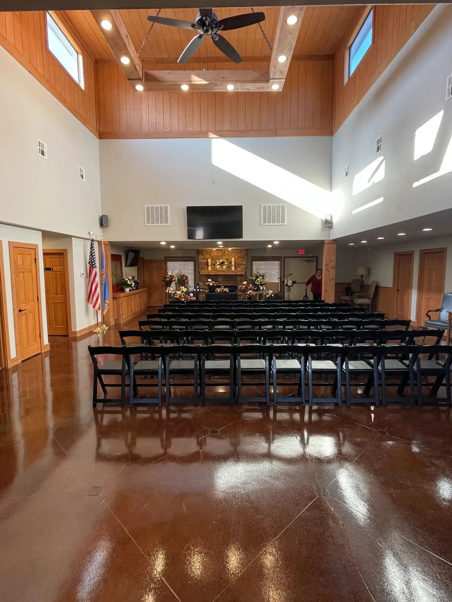 Empty church hall with rows of chairs, wooden ceiling, and sunlight streaming across the floor