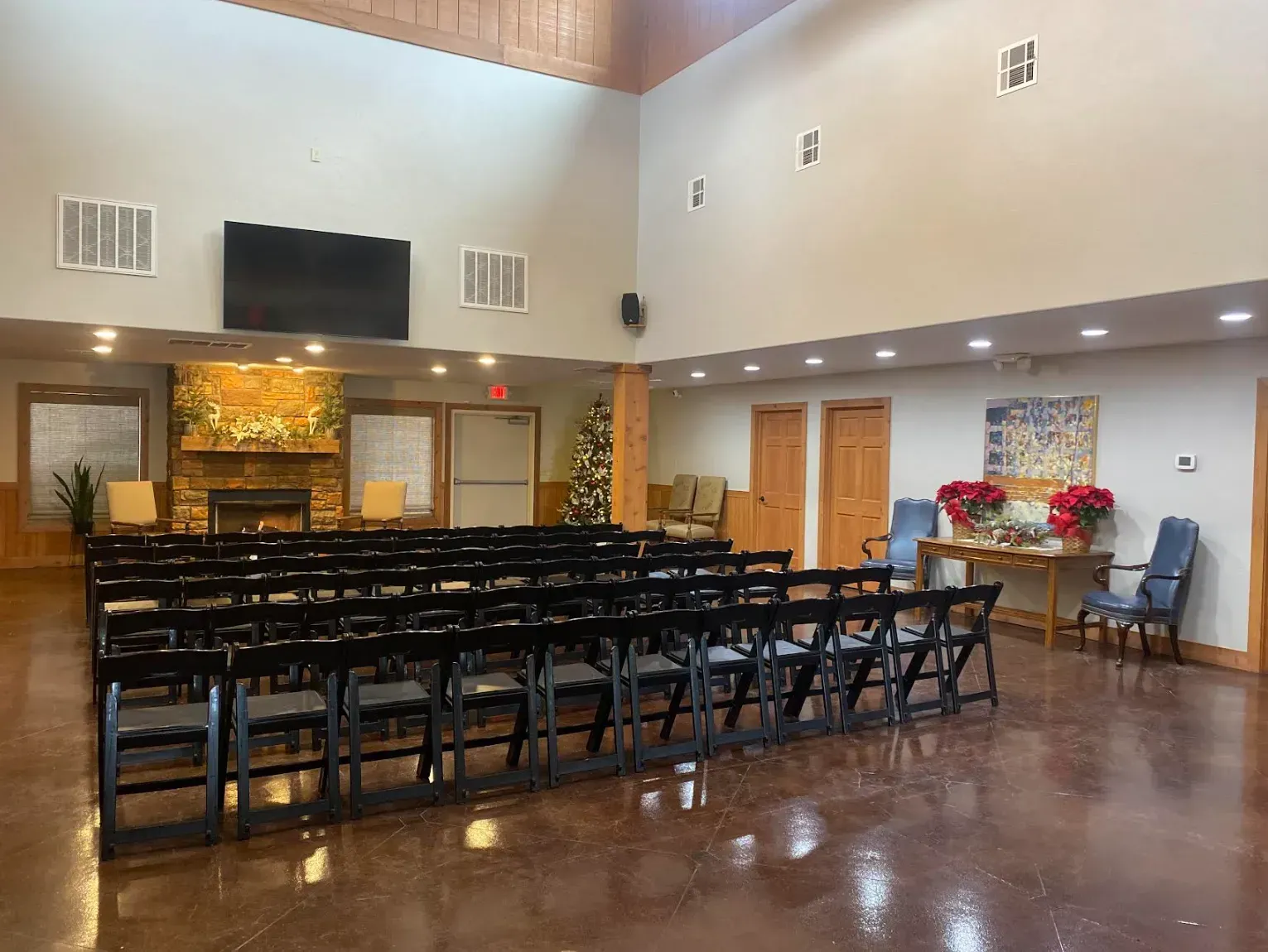 Empty hall with rows of black chairs, polished floor, and a small decorated table near double doors.