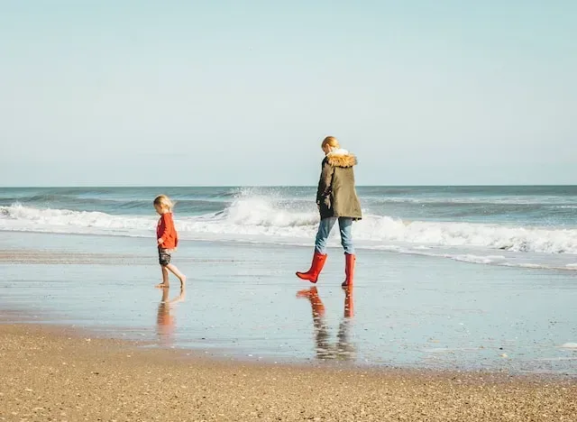 Two people walking along a beach with waves and reflections on wet sand