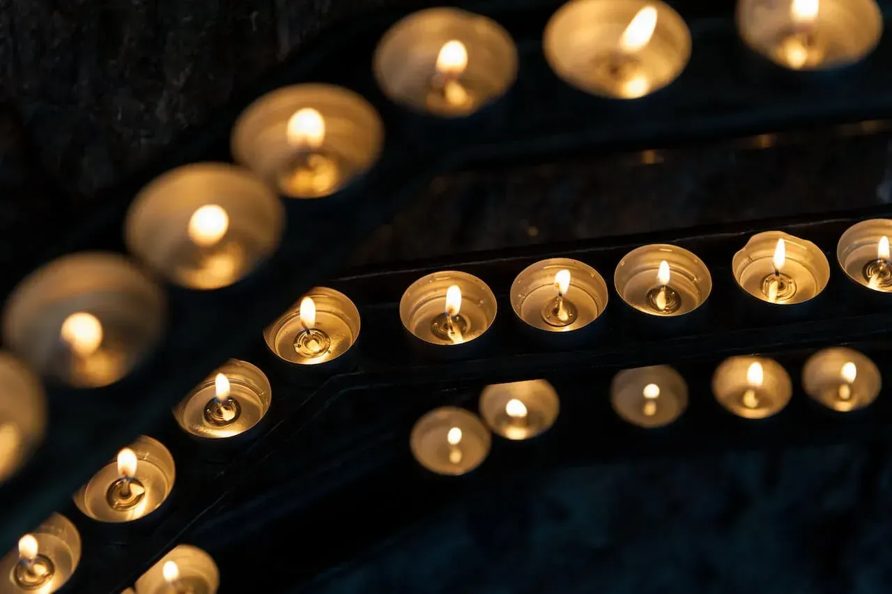 Rows of warm glowing candles in a dark setting, creating a soft golden light pattern