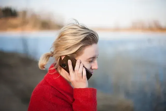 Person in a red sweater talking on a phone by a lake