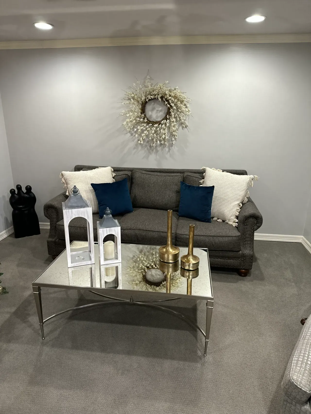 Gray living room with sofa, silver coffee table, decorative pillows, and wall wreath decor