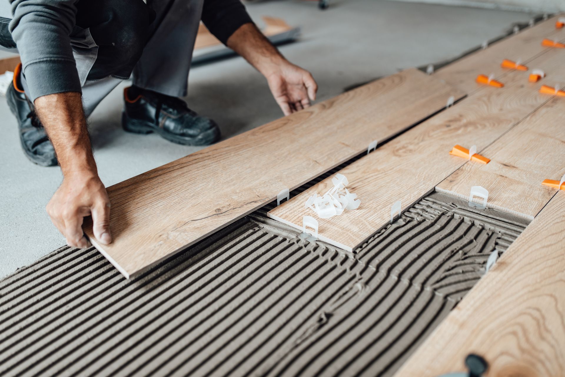 A man installs wooden flooring, kneeling on the ground with tools and planks around him.