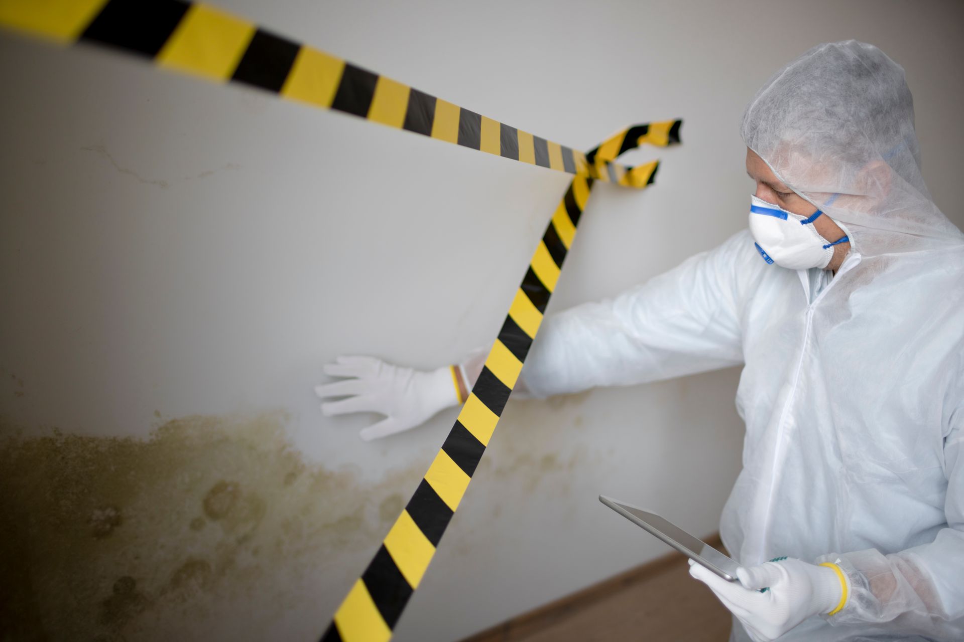 A mold remediation technician in a protective suit inspecting and containing mold damage on an interior wall.