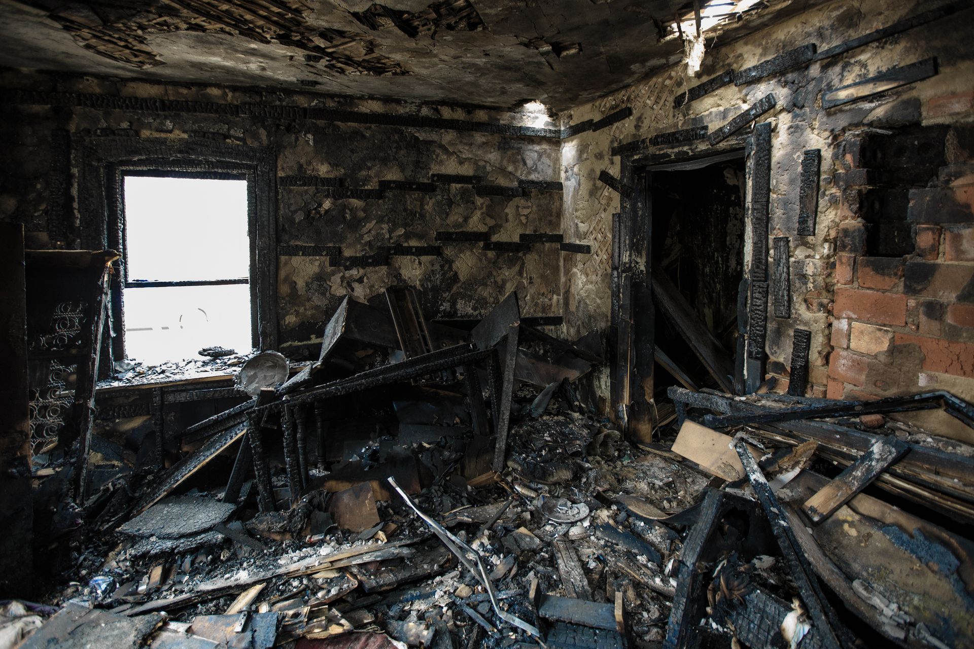 Charred room interior after a fire; debris and damaged walls surround a window and doorway.