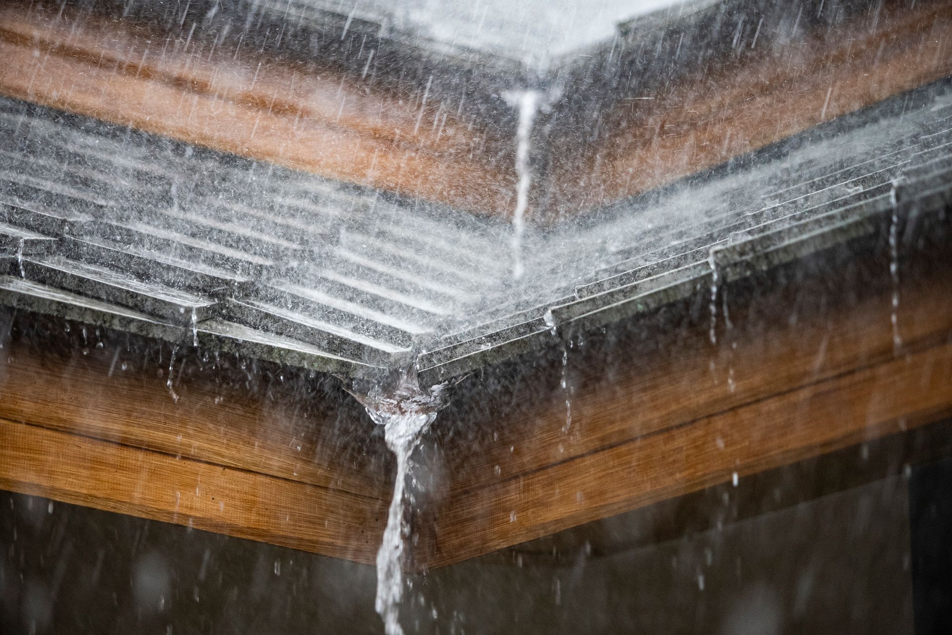 Rainwater pouring from a gutter on a wooden roof.