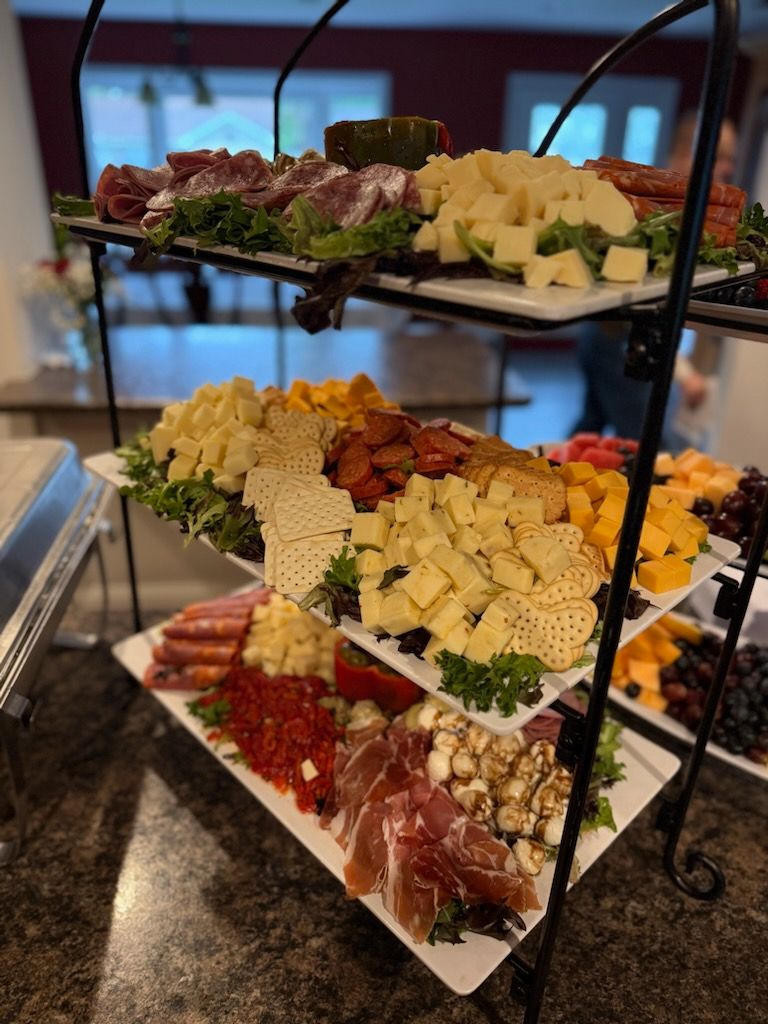 Three-tiered charcuterie board with meats, cheeses, and fruits on white platters.