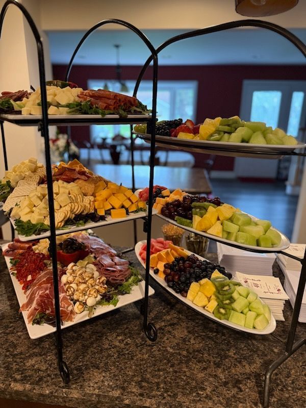 Three-tiered food display with various fruits, vegetables, and charcuterie on plates. Indoors with a blurred background.
