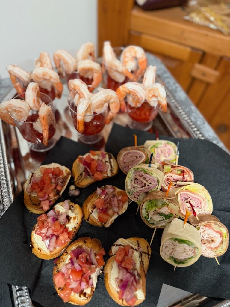 Appetizers: Shrimp cocktail in cups, bruschetta, and wrap pinwheels on a silver tray.