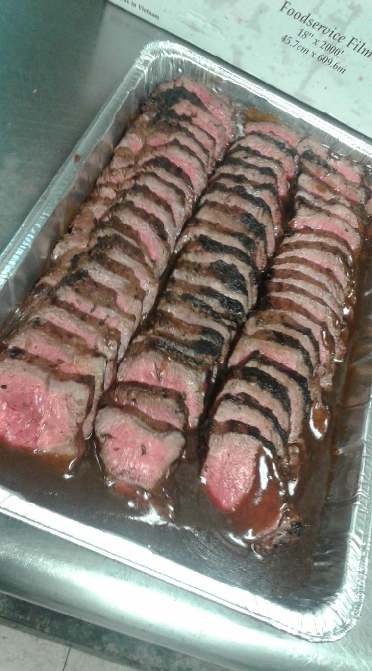 Sliced grilled steak in a foil pan, medium-rare with a brown sauce.