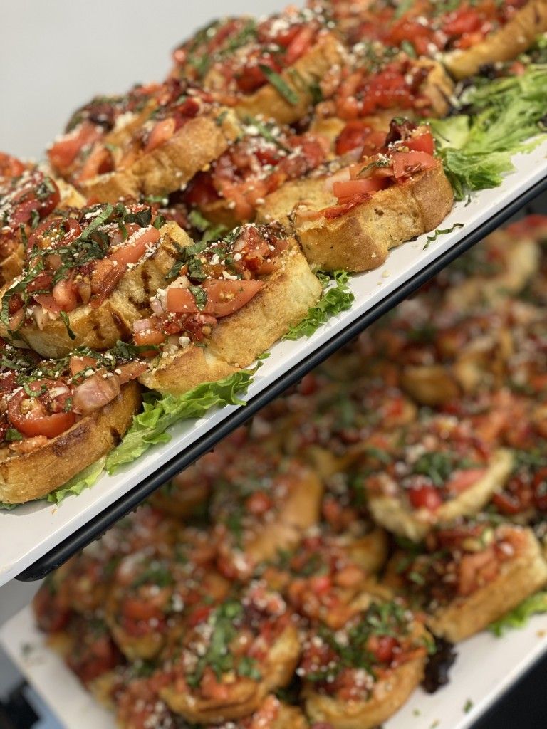 Bruschetta appetizers on white platters, featuring toasted bread topped with tomatoes, herbs, and cheese.