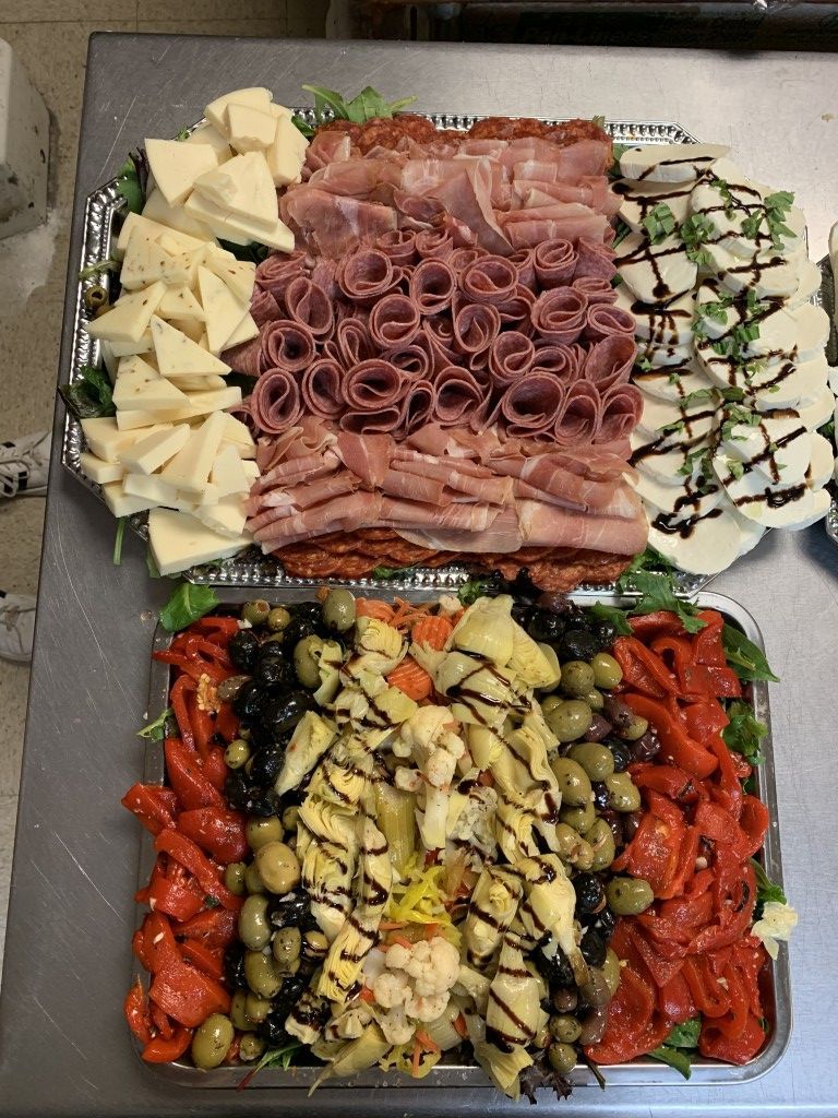 Two platters of food: meats, cheeses, olives, artichokes, and roasted peppers arranged on a table.