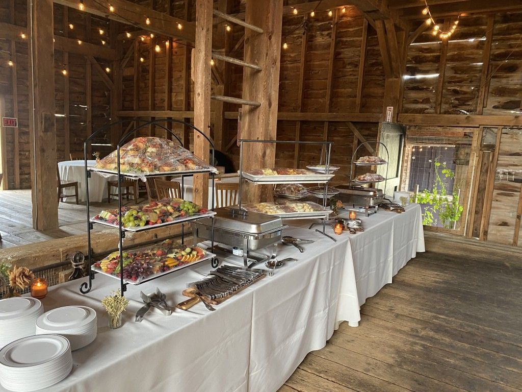 Buffet table in a rustic barn with various dishes and serving platters on a white tablecloth.