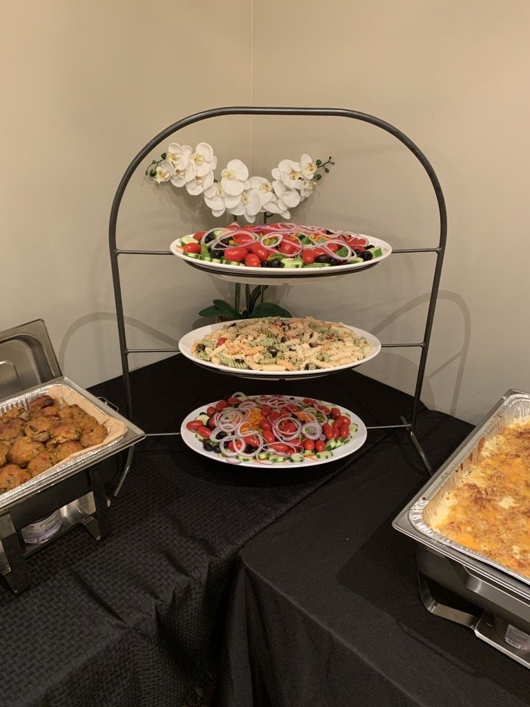 Buffet with pasta dishes on tiered server, plus two chafing dishes with food on black tablecloth.