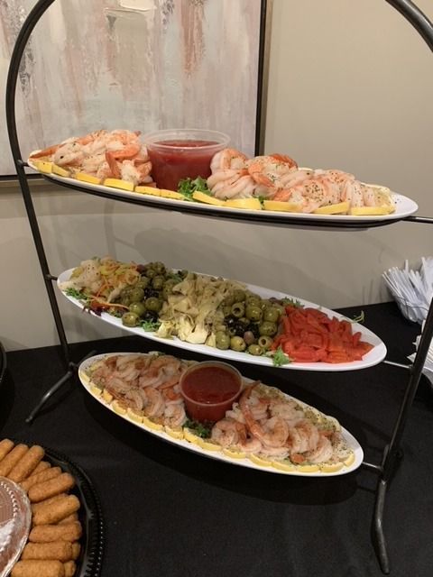 Three-tiered serving stand with shrimp cocktail, olives, and other appetizers on white platters.
