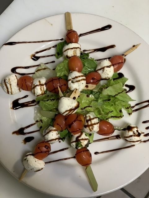 Caprese skewers with mozzarella, tomatoes, and balsamic glaze on a bed of lettuce, plated on white.