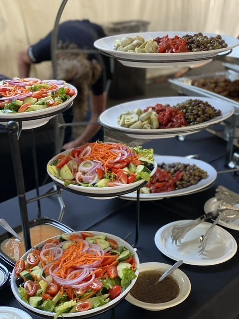 Salads on tiered display. Vegetables, lentils, and dressings on white plates. Someone in the background.