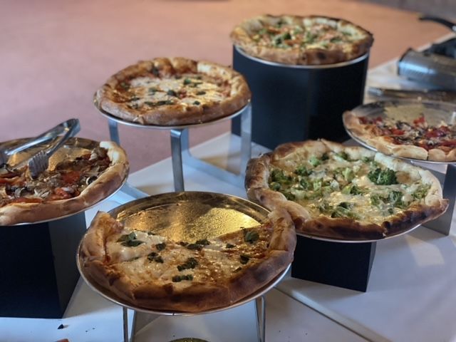 Pizzas on display at an event. Various toppings, on pedestals, set against a blurred background.