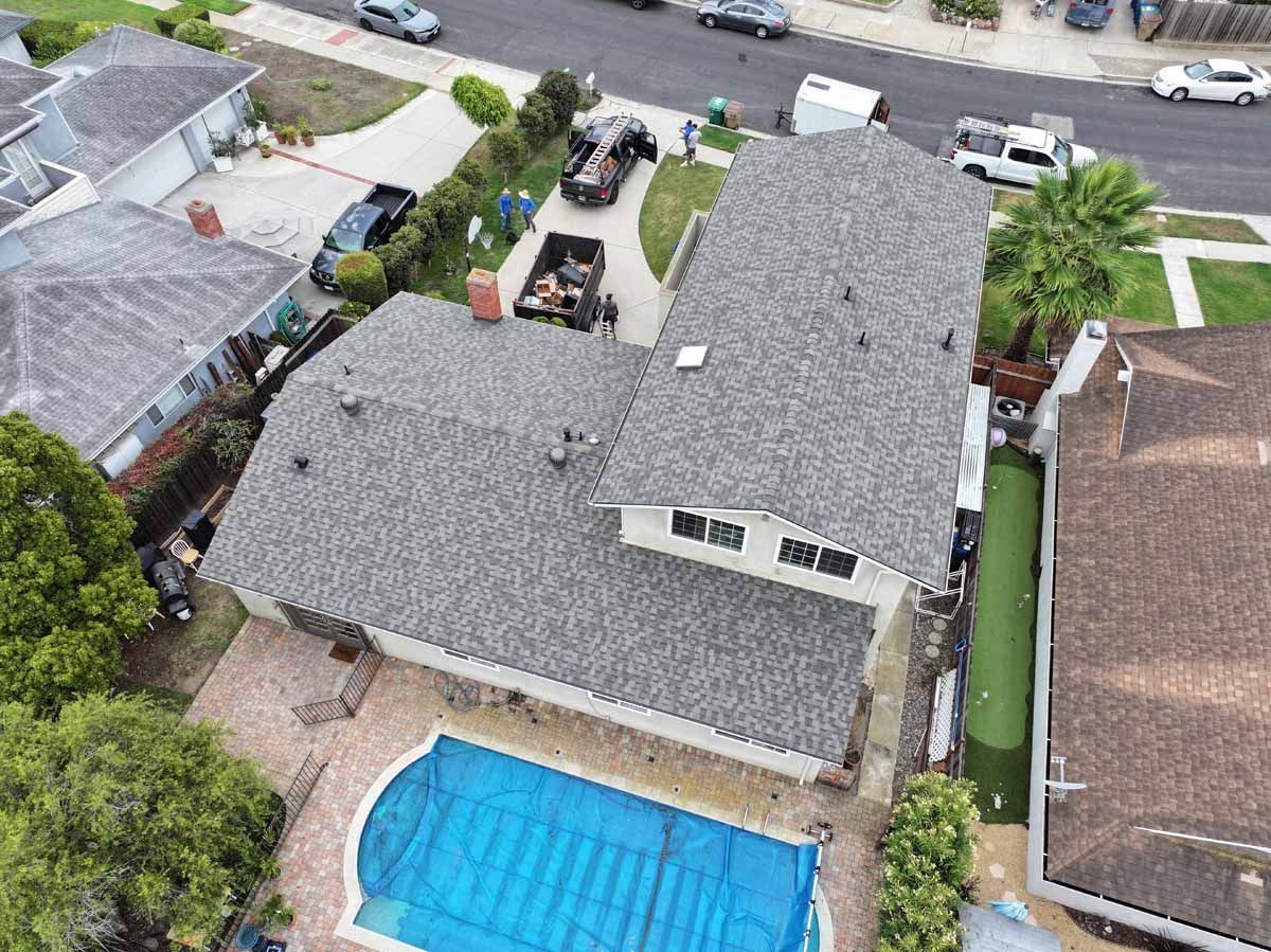 Aerial view of a suburban house with a gray roof, backyard pool, and neighboring homes