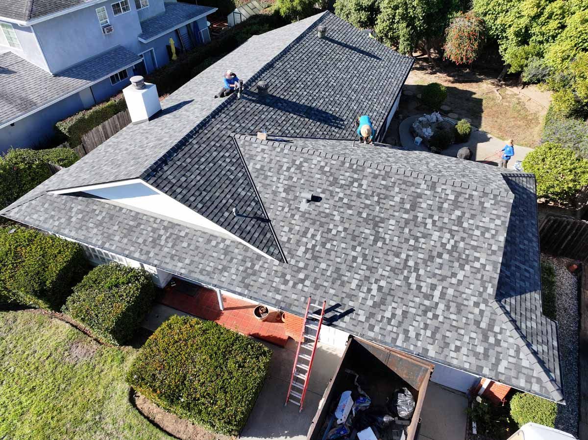 Aerial view of a gray shingled house roof with chimneys and surrounding trees
