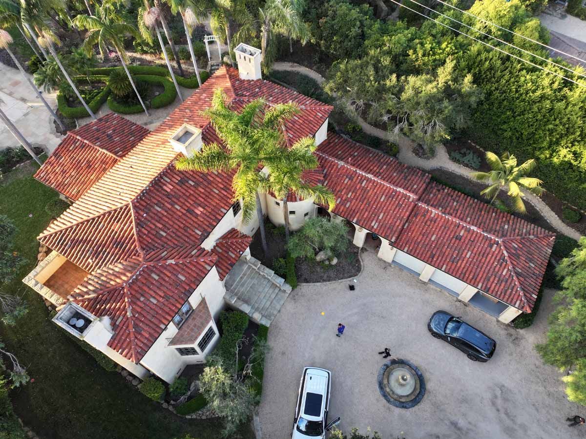 Aerial view of a red-tiled house with a courtyard, parked cars, and surrounding palm trees