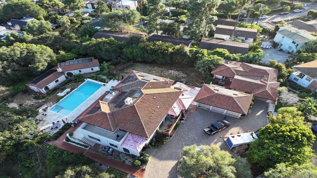 Aerial view of a resort with a large swimming pool, tiled-roof buildings, and surrounding trees