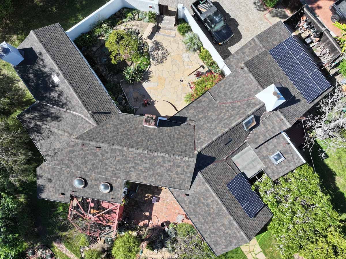 Aerial view of a house roof surrounding a courtyard with parked cars and green landscaping