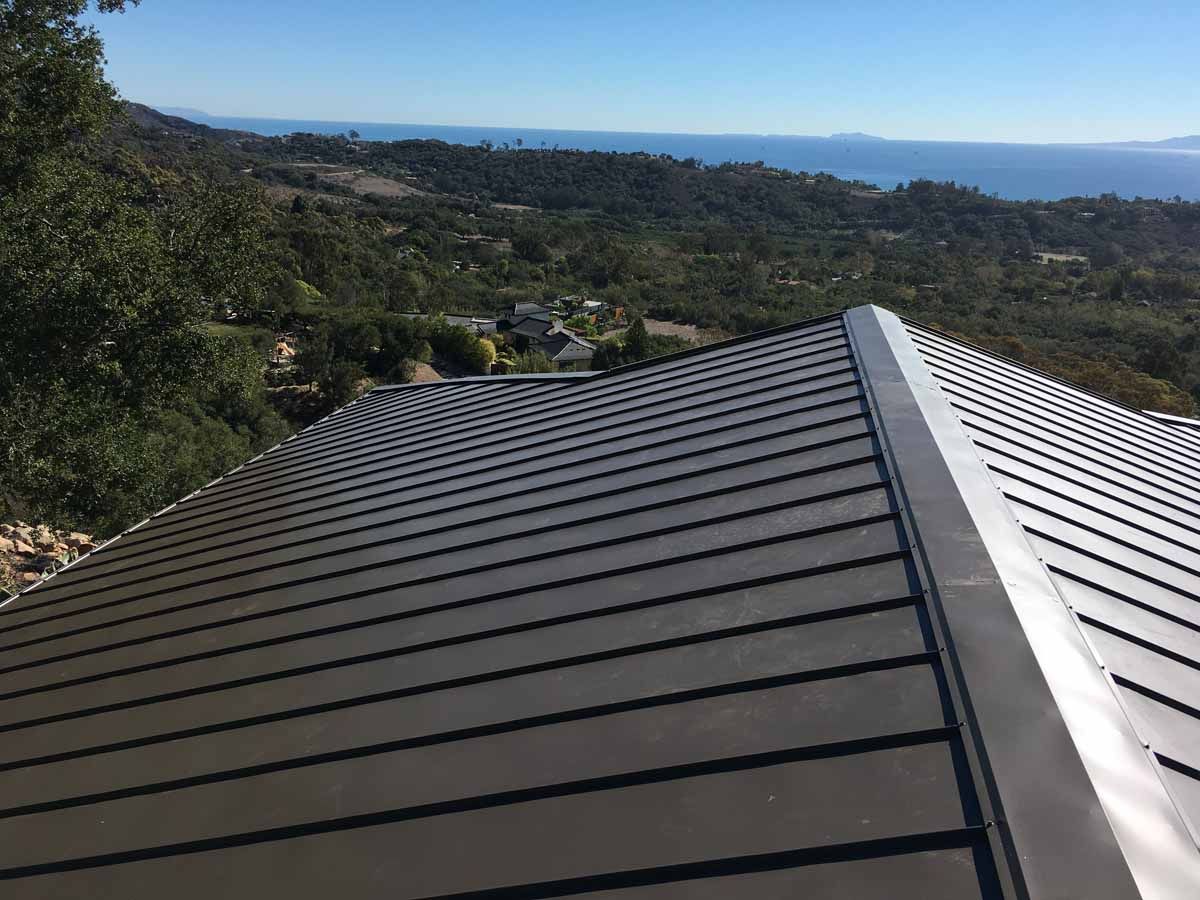 Dark metal roof overlooking a wooded hillside and distant ocean under clear blue sky