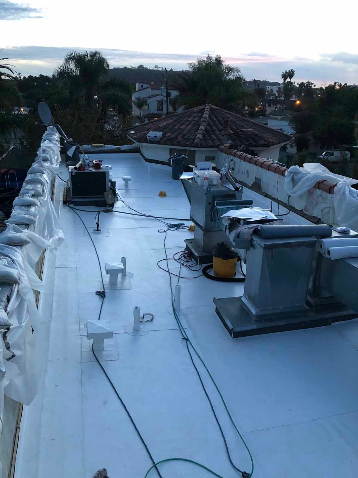 Rooftop with white waterproof coating, vents and cables, at dusk with palm trees in the background