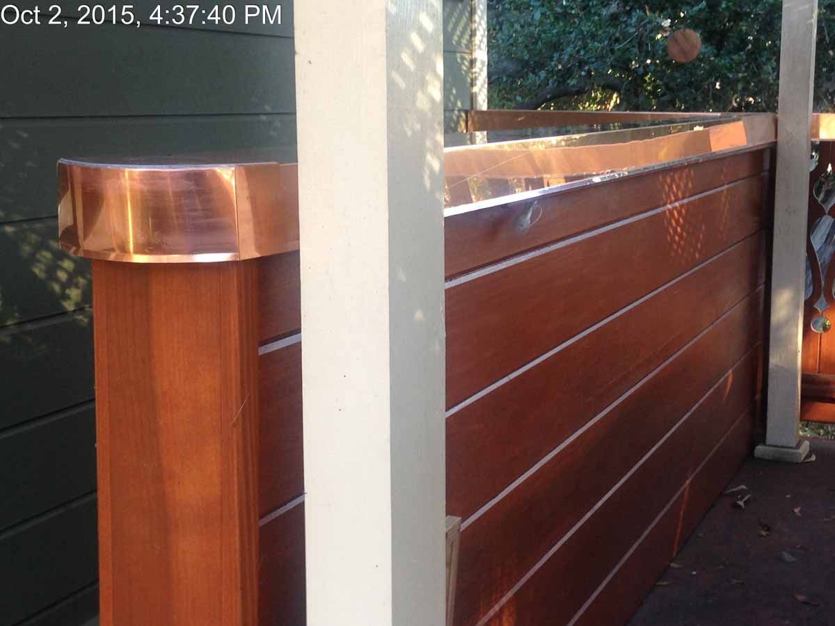 Copper-topped wooden railing beside a white post on an outdoor deck or walkway.