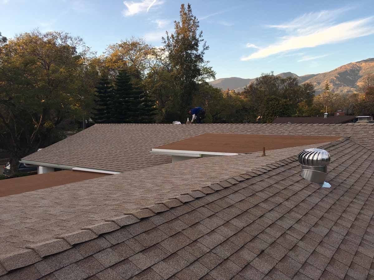 Roofing workers replacing shingles on a house roof in a wooded hillside neighborhood