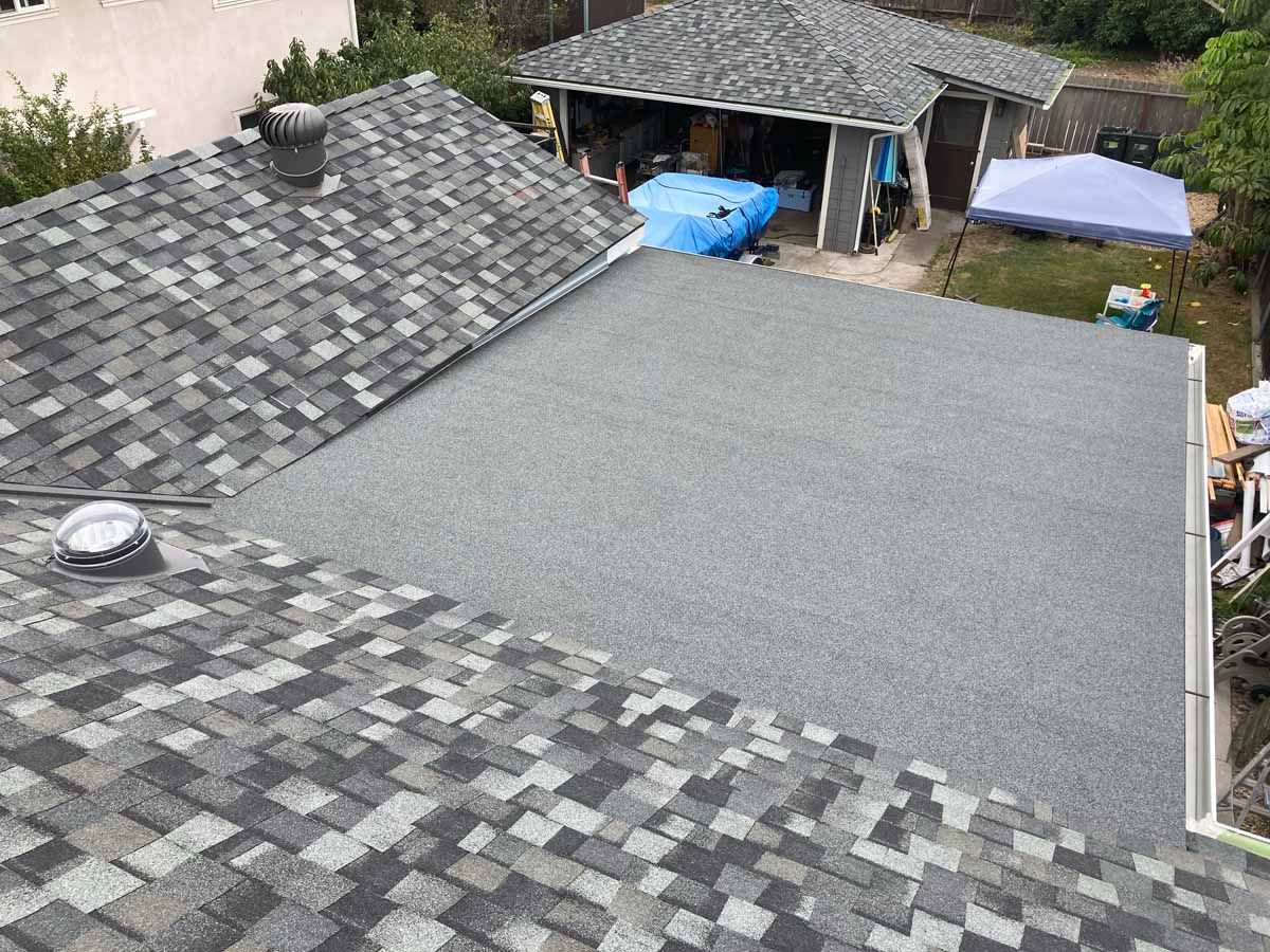 Rooftops with gray shingles beside a covered patio and yard area with a blue tarp