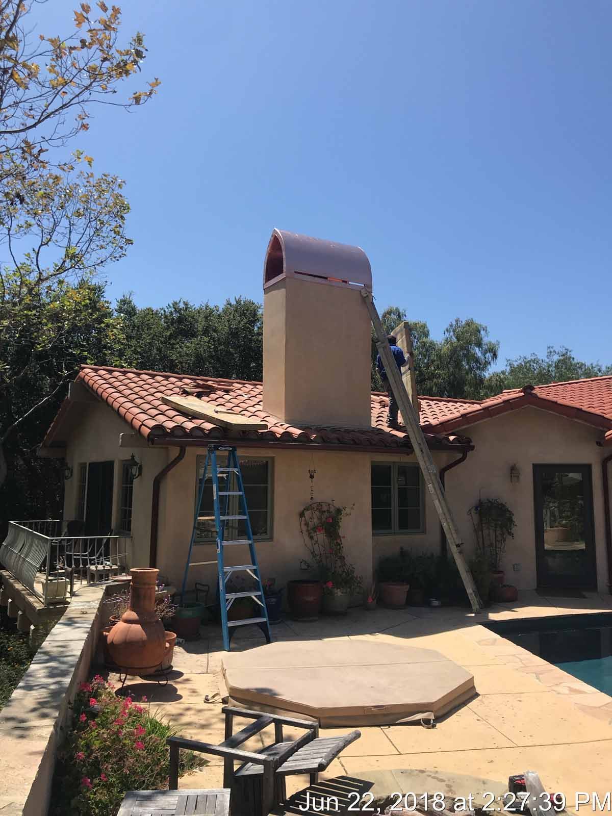 House roof being repaired, with a ladder and a tall vent or chimney under a clear blue sky.