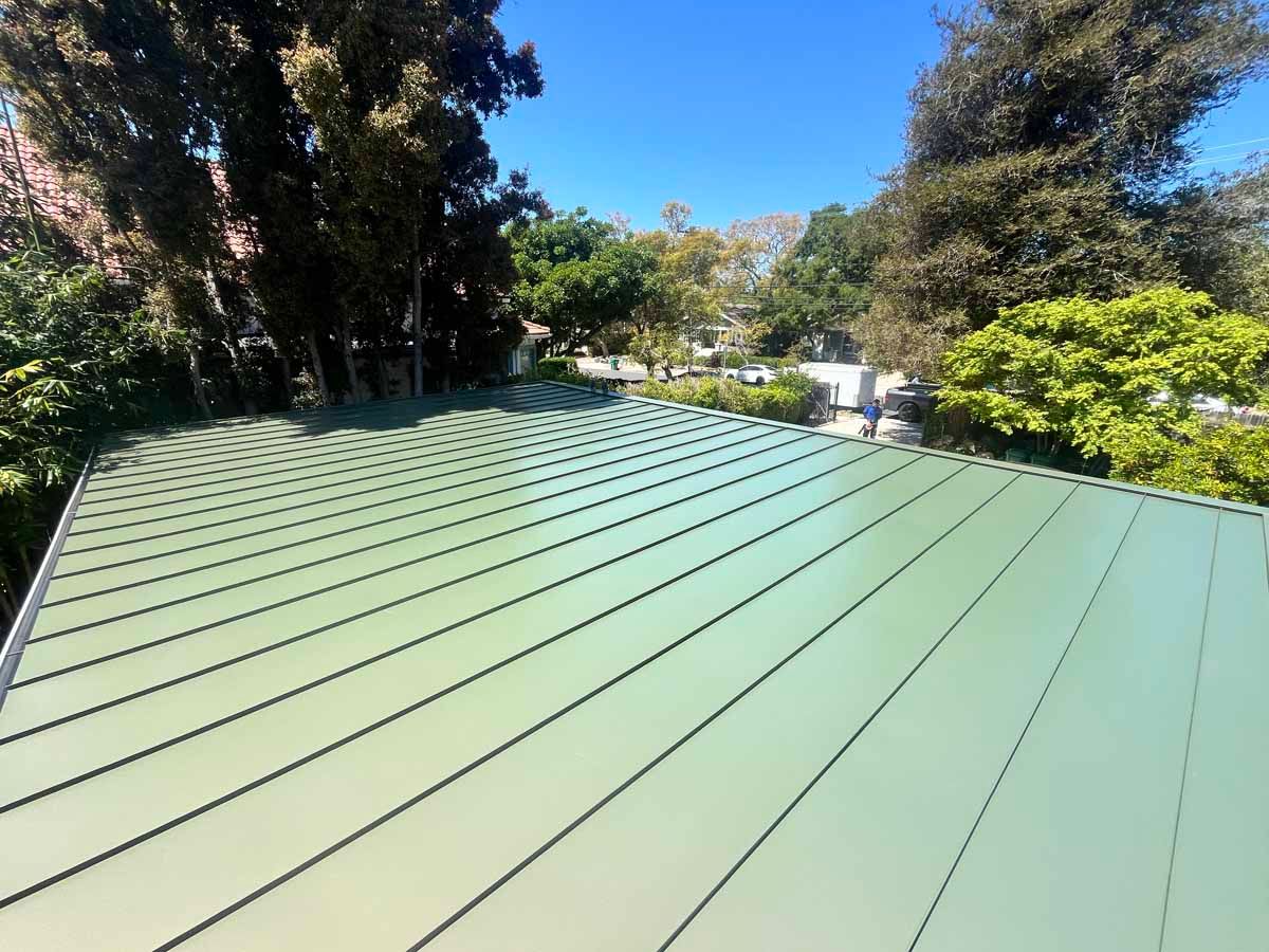 Green metal roof with standing-seam panels, viewed from above with trees in the background