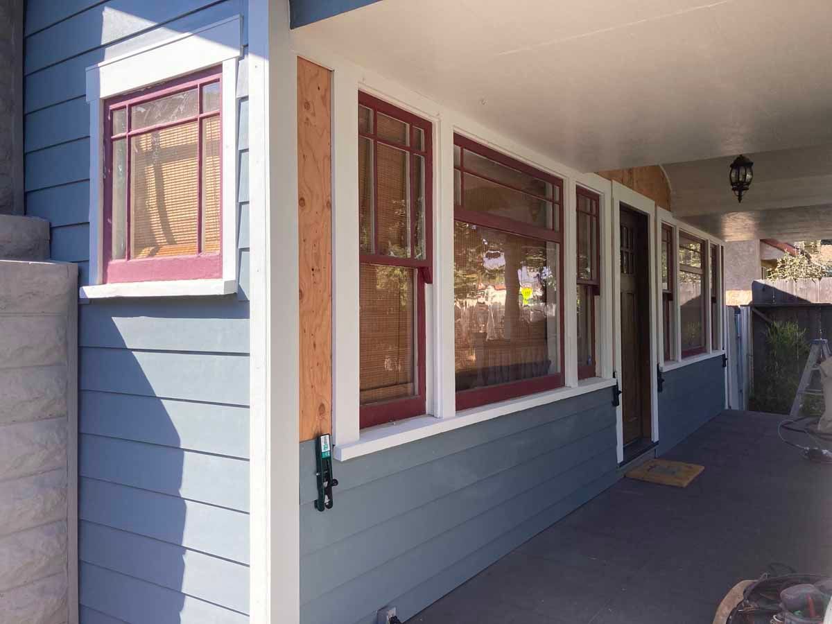 Covered apartment walkway with blue siding, windows, and a front door beside the porch railing