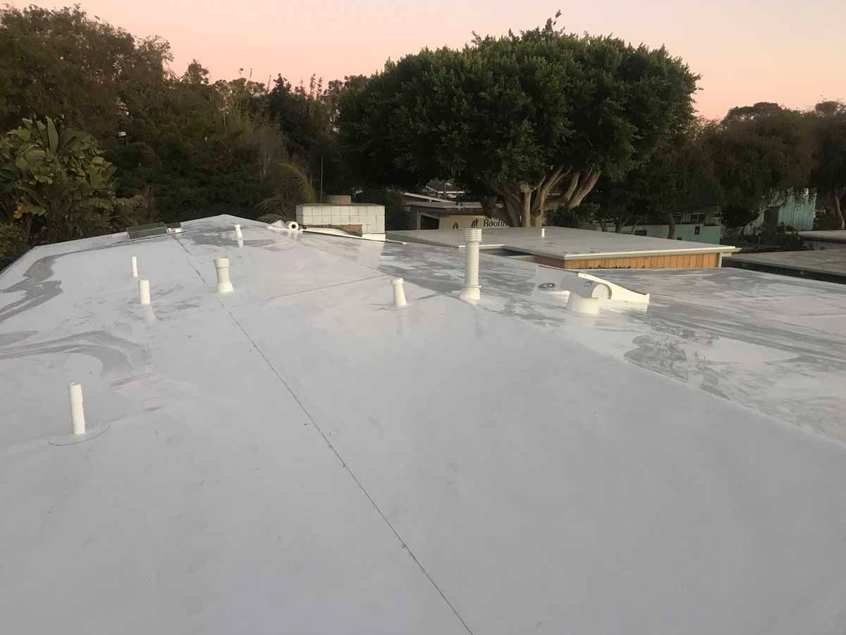 Flat white rooftop at sunset with vents and trees in the background