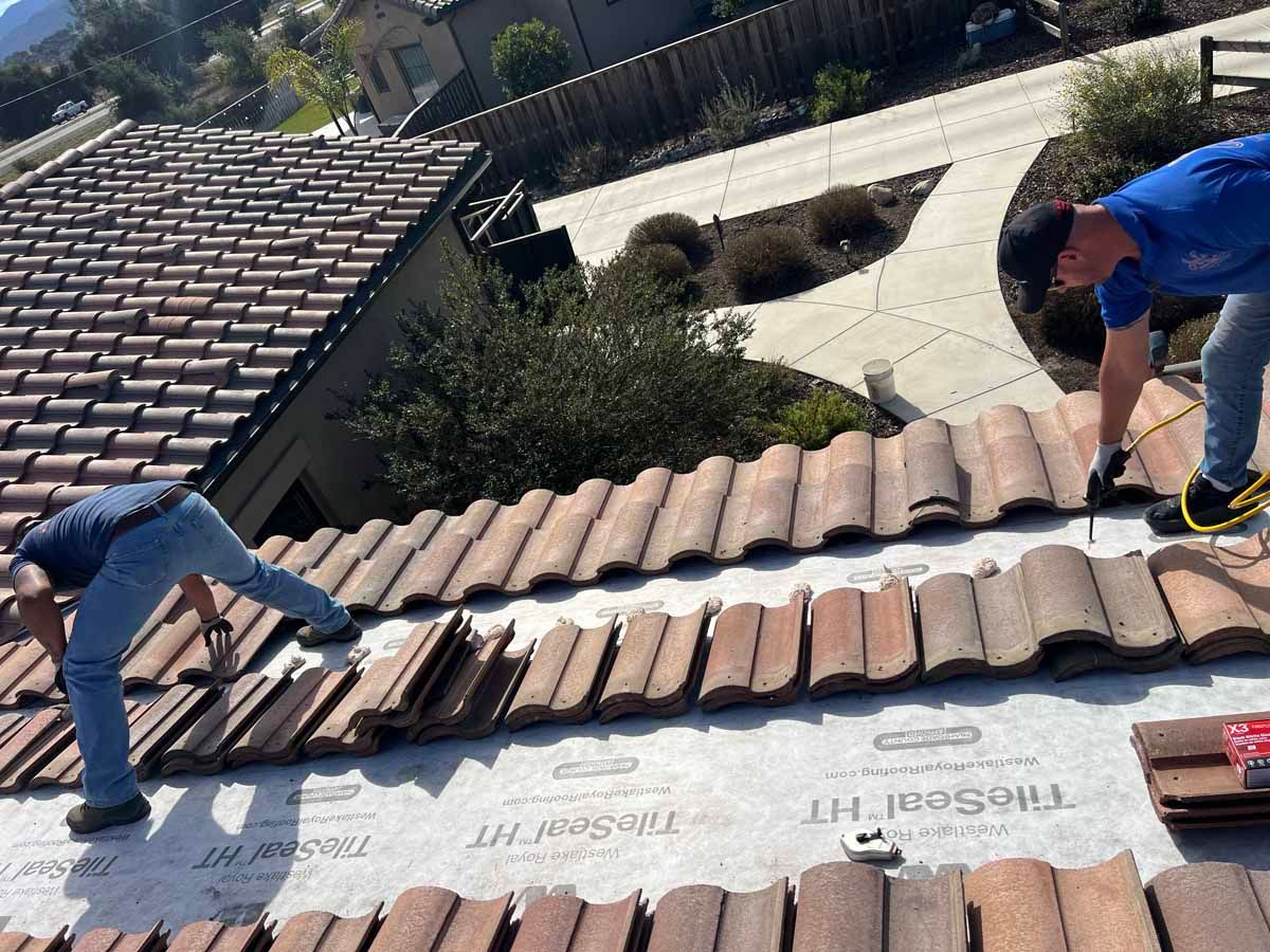 Two workers installing roof tiles on a sloped house roof on a sunny day