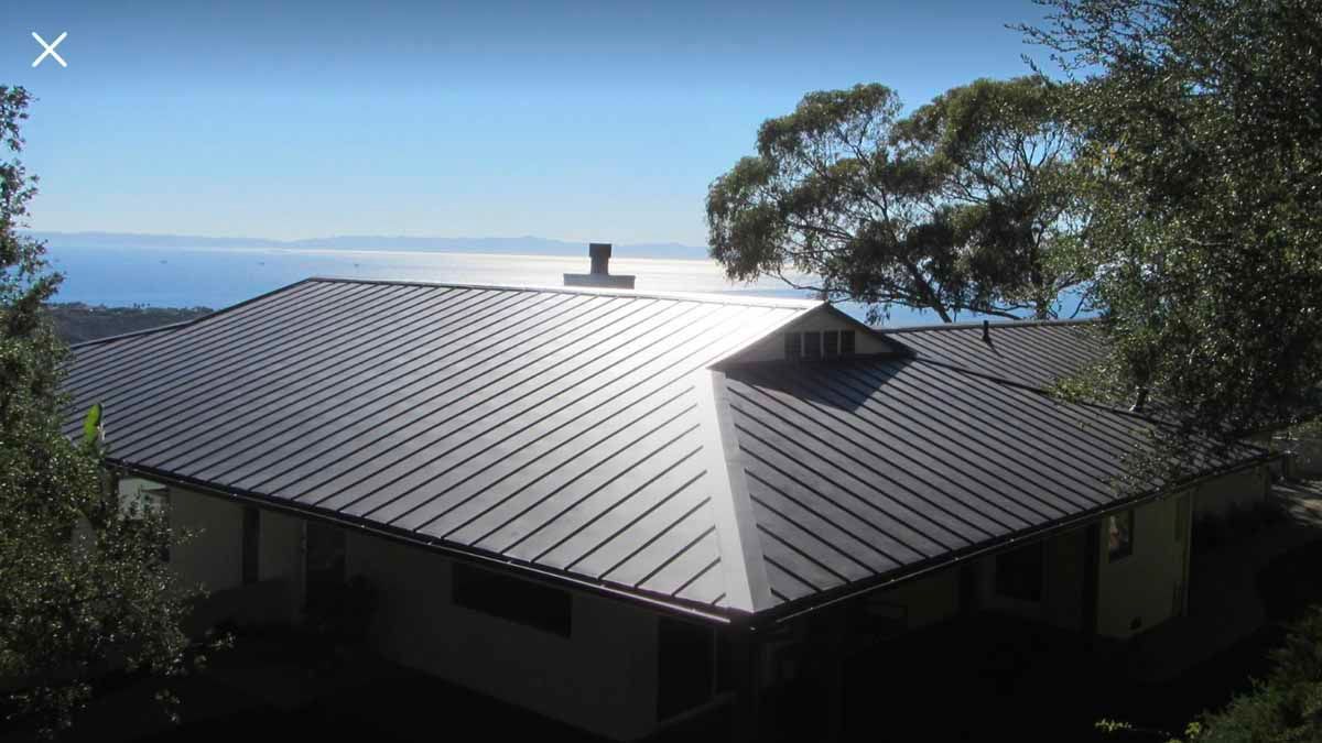 Metal roof on a house overlooking the ocean, with trees in the foreground and sunlight reflecting off the roof.
