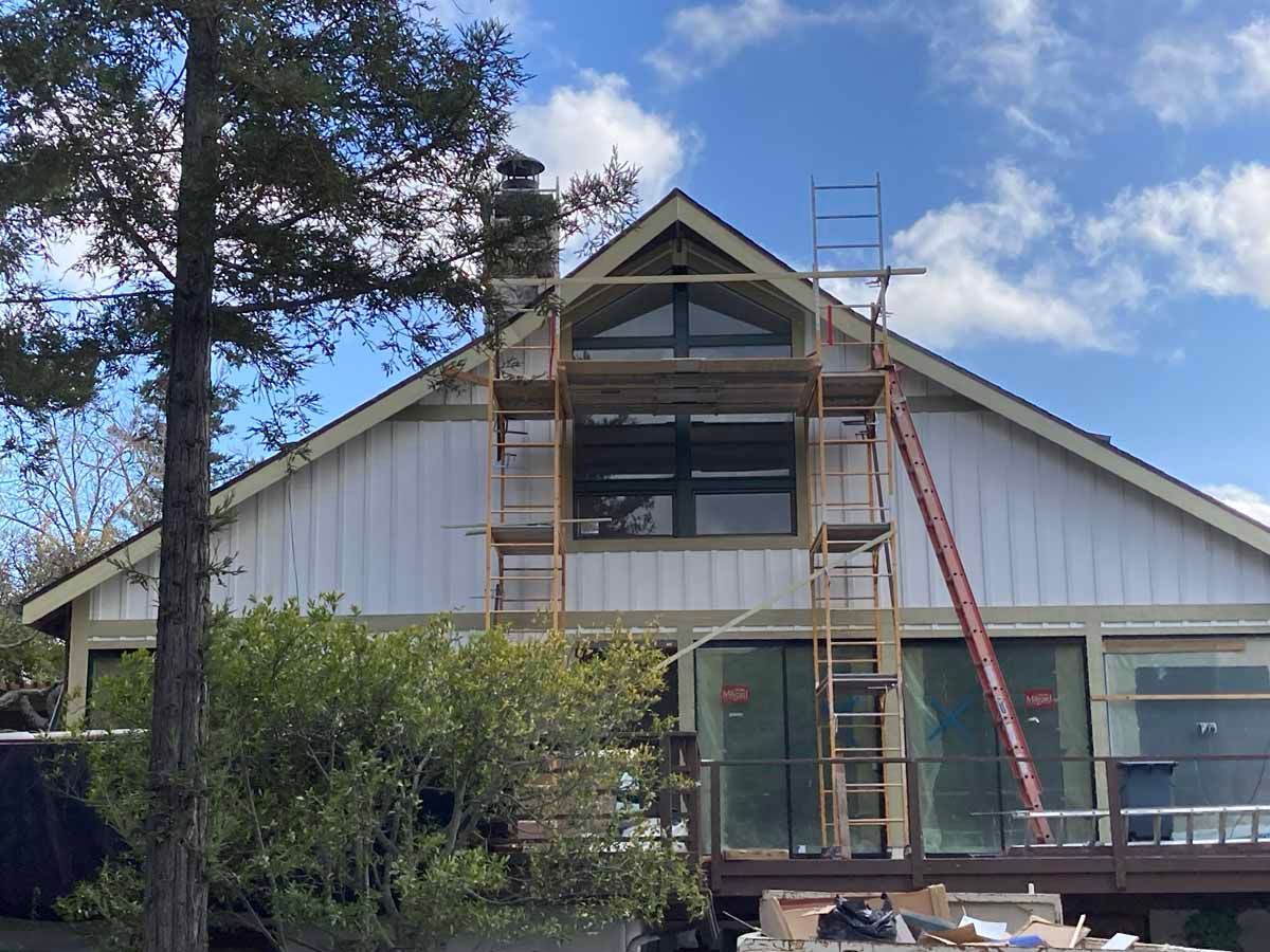 House exterior with ladders and scaffolding under a partly cloudy sky