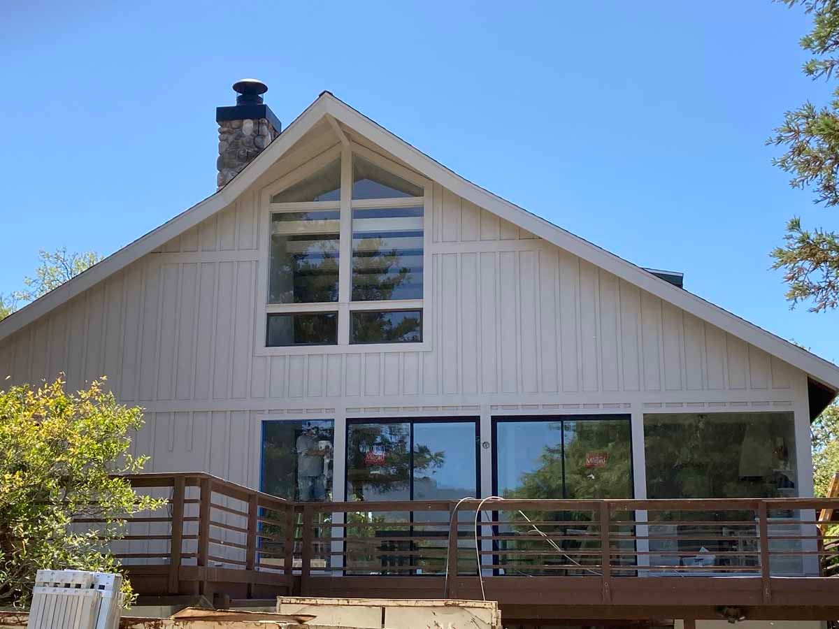 White house with large windows, gabled roof, and wooden deck under a clear blue sky