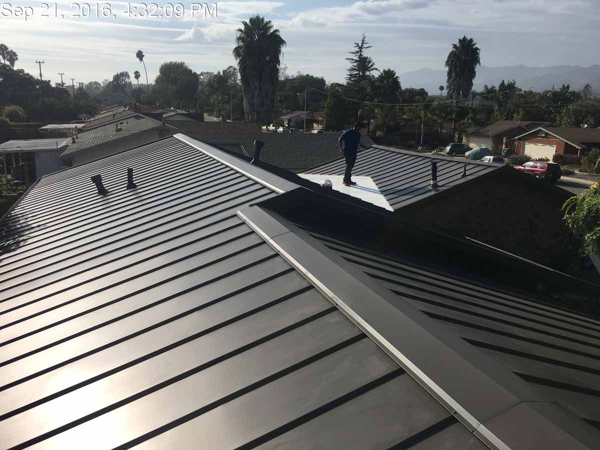 Metal roofs under construction with a worker standing on the ridge in bright daylight